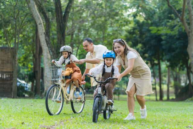 Happy,Asian,Parents,Teaching,Their,Little,Daughter,To,Ride,A